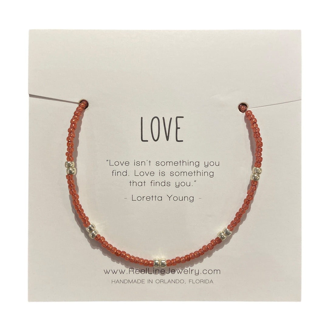 The "Love - Pomegranate and Silver" bracelet by Reel Line Jewelry is a thin, beaded piece on a card with an inspirational quote on love by Loretta Young, handcrafted in Orlando with adjustable links.
