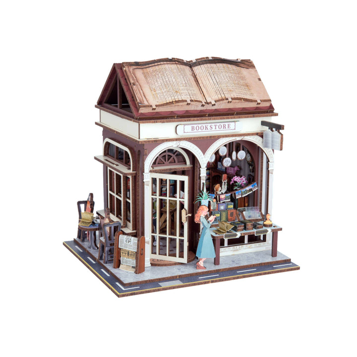 The Hands Craft DIY Miniature House Kit: Bookstore features a cozy shop with arched windows, outdoor books, a table and chairs, and an apron-clad figure arranging items—ideal for cottagecore fans.