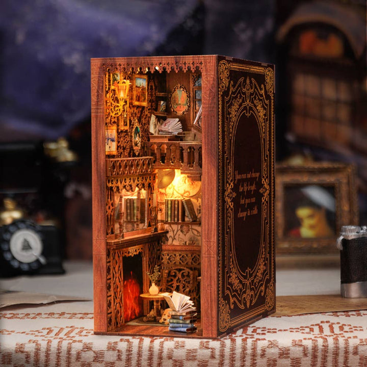 The Hands Craft DIY Book Nook Kit: Eternal Bookstore features a magical miniature library with tiny books, shelves, a glowing lamp, and cozy reading nook—all protected by a dust cover in an ornate book-shaped case.