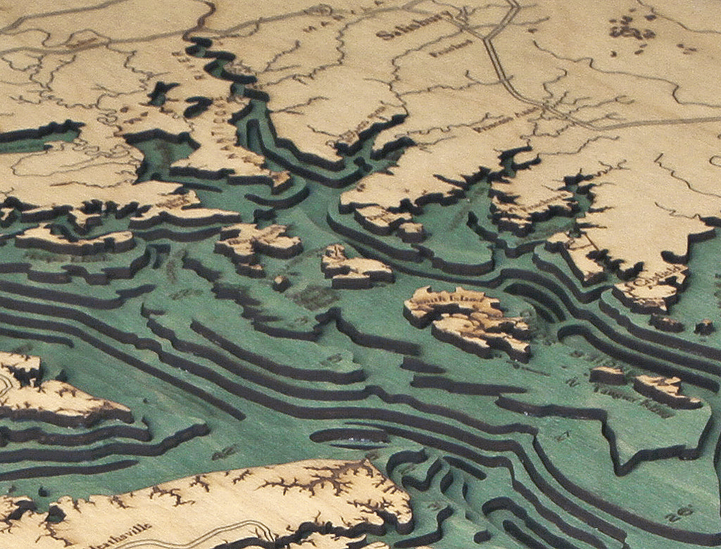 The WoodChart Chesapeake Bay 24.5" x 31" Black Frame displays a detailed wooden topographic map with layered cutouts showing coastlines, elevation changes, and labeled regions and bodies of water.
