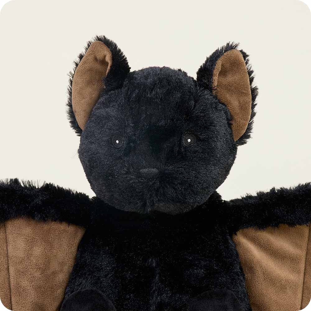 The Bat Warmie from Warmies is a plush black bat with a fuzzy texture, showcasing large ears and wings, and featuring a beige inner lining on the ears and wings. It is displayed against a plain background.