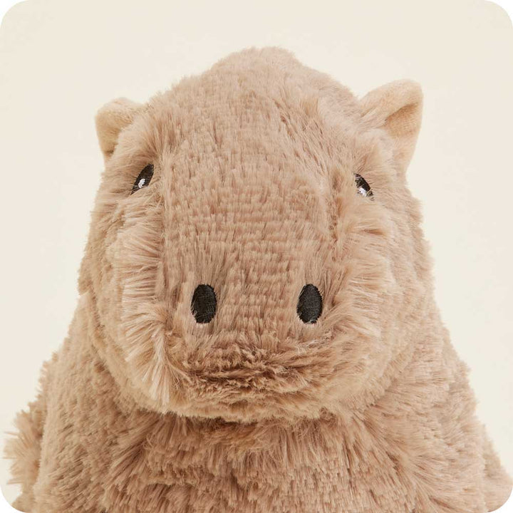 A close-up of the Capybara Warmie by Warmies showcases its plush, soft texture and neutral beige hue. The toy features black eyes and small ears, giving it an adorable and cuddly look against a plain light-colored background.