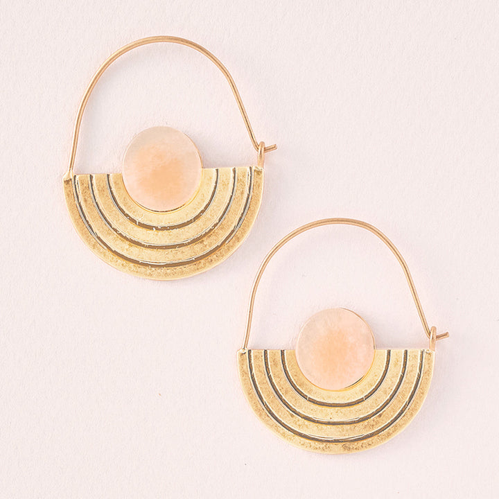 The Stone Orbit Earring Sunstone Gold by Scout Jewelry is designed with hypoallergenic 14K gold dipped metal and showcases semicircular pendants that boast a layered design with a central sunstone. The hoops feature elegant geometric concentric lines against a light, textured background.