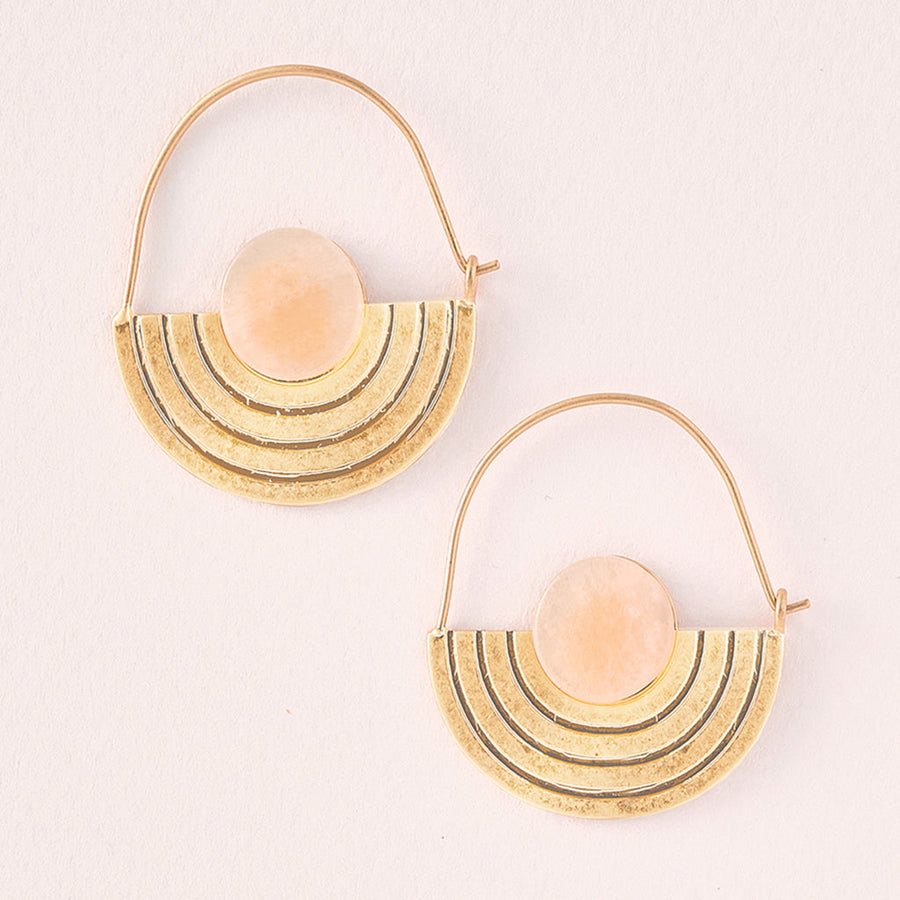 The Stone Orbit Earring Sunstone Gold by Scout Jewelry is designed with hypoallergenic 14K gold dipped metal and showcases semicircular pendants that boast a layered design with a central sunstone. The hoops feature elegant geometric concentric lines against a light, textured background.