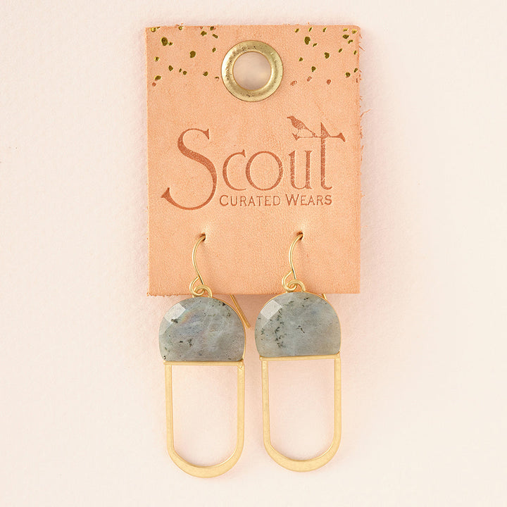 The "Modern Stone Earring Labradorite Gold" by Scout Jewelry is a pair of hypoallergenic earrings featuring labradorite stones, displayed on a tan cardboard backing labeled with the brand name. These earrings showcase a geometric design with a semicircular stone and an elongated, rectangular gold metal loop.