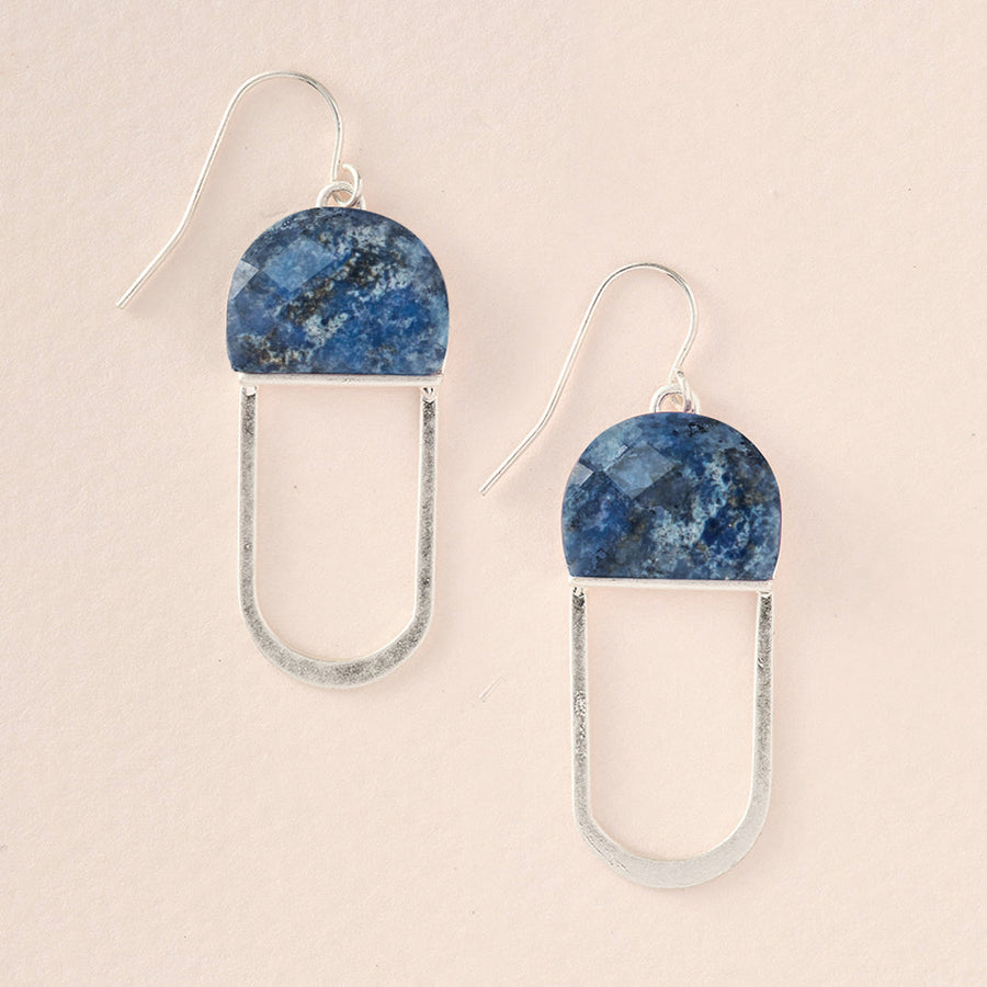 The Modern Stone Earring Lapis Silver by Scout Jewelry features a semi-circular dark blue lapis stone with a silver hook. Below each stone, a thin silver oval loop hangs, creating a minimalist and modern aesthetic. These lightweight and hypoallergenic earrings are beautifully displayed on a light beige background.