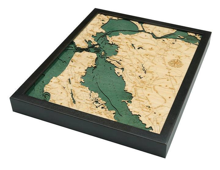 The WoodChart San Francisco Bay 16" x 20" Black Frame is a layered 3D wood map showing the Bay Area with light wood land, teal water, engraved geographic details, and a compass rose for a nautical look.