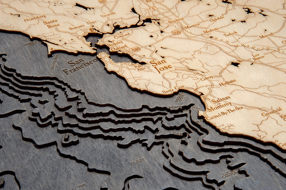 The WoodChart California Coast 24.5" x 31" Grey Frame is a laser-cut wooden map detailing land and underwater topography near San Francisco and San Jose, with engraved city names for added precision.
