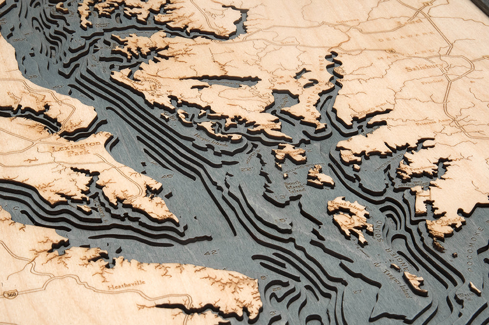 The WoodChart Chesapeake Bay 24.5" x 31" Grey Frame is a wooden topographic map with engraved place names, roads, detailed elevation layers, and geographic features showing coastal inlets and water depths.