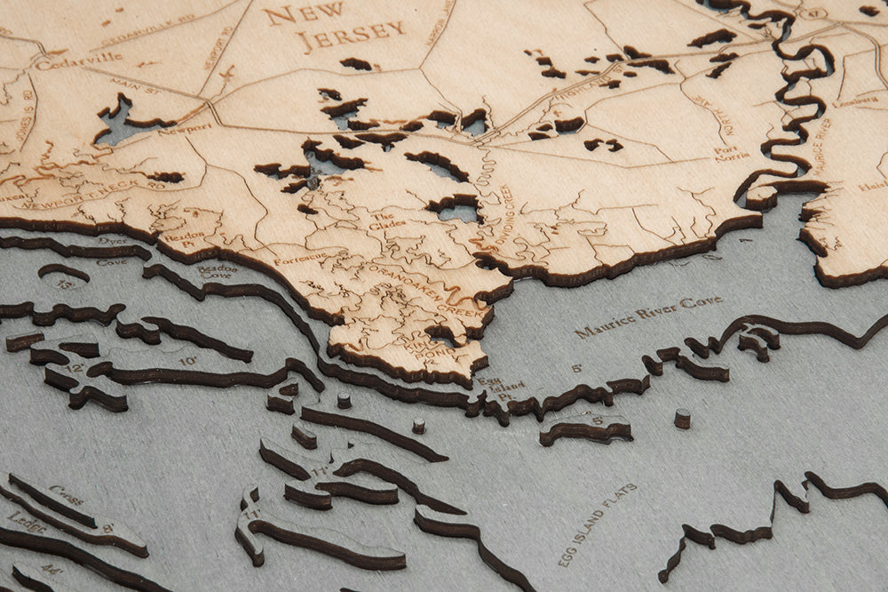 A close-up of the WoodChart Deleware Bay 24.5 x 31 Grey Frame laser-cut wooden map, highlighting the southern New Jersey coastline with detailed land and water features, including Maurice River Cove.