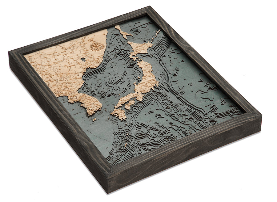 The WoodChart Japan Korea 16" x 20" Grey Frame features a layered wood map with light wood land, darker textured ocean depths, and finely engraved details including a compass rose.