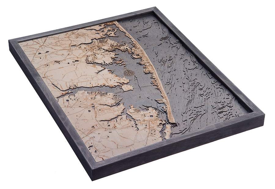 The WoodChart Ocean City MD 24.5 x 31 Grey Frame features a layered woodcut map with tan and dark gray contrasts, highlighting coastal topography and detailed contours of land and water.