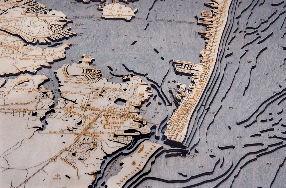 The WoodChart Ocean City MD 24.5 x 31 Grey Frame features a detailed wooden map with engraved streets, waterways, and coastal layers of West Ocean City and Ocean City, Maryland, in varied textures.