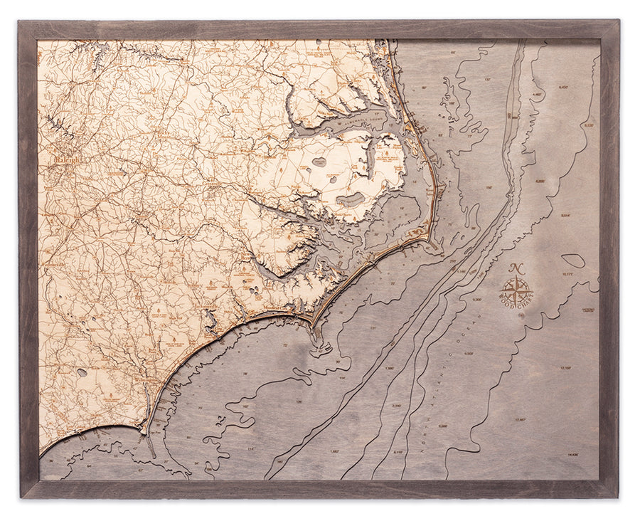 The WoodChart North Carolina Coast 24.5" x 31" map features detailed engravings of the eastern coastline, rivers, and roads—including the Outer Banks—with a compass rose and comes framed in elegant grey.