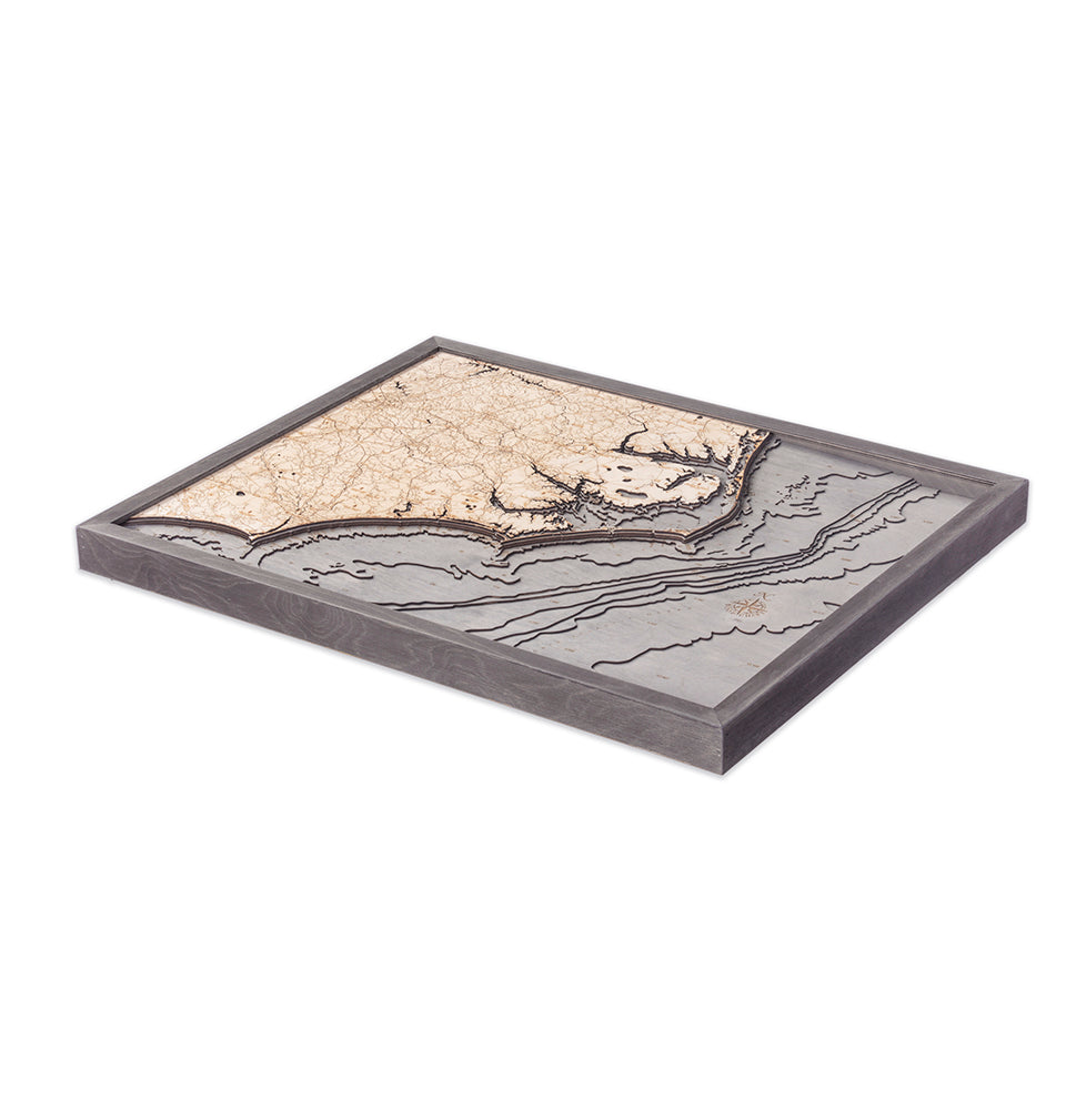 The WoodChart North Carolina Coast 24.5" x 31" features a framed, three-dimensional wooden map with detailed beige and gray contours, highlighting land and water areas. The elegant grey frame adds a stylish touch.