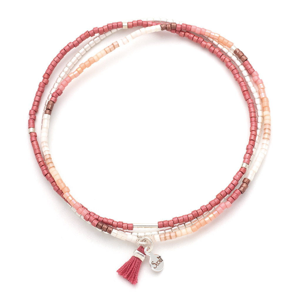 The Blush Multi Silver Miyuki Bracelet Trio from Scout Jewelry is a multi-strand stacking bracelet, adorned with small pink, white, and brown Miyuki Delica beads. It features a small metal charm engraved with "Soul" and is embellished with a pink tassel attached to its stretch cord.