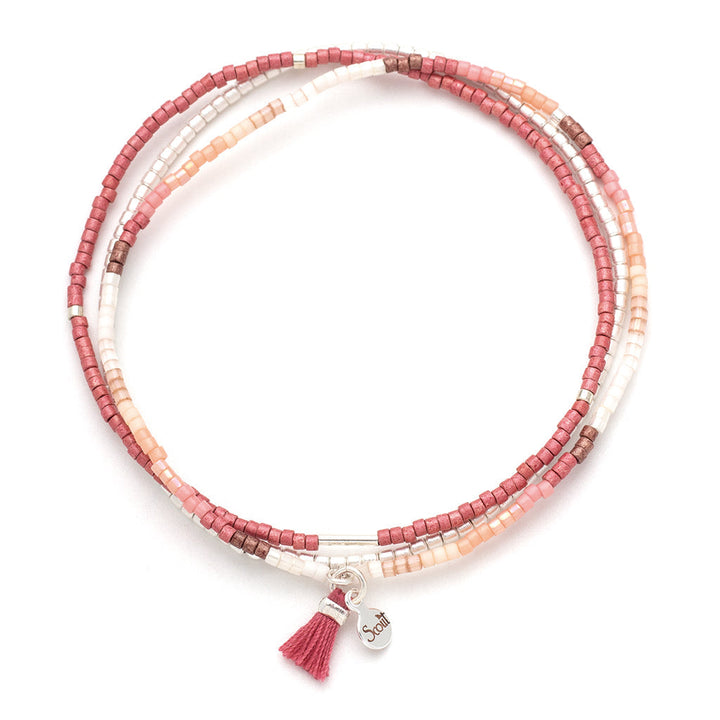 The Blush Multi Silver Miyuki Bracelet Trio from Scout Jewelry is a multi-strand stacking bracelet, adorned with small pink, white, and brown Miyuki Delica beads. It features a small metal charm engraved with "Soul" and is embellished with a pink tassel attached to its stretch cord.