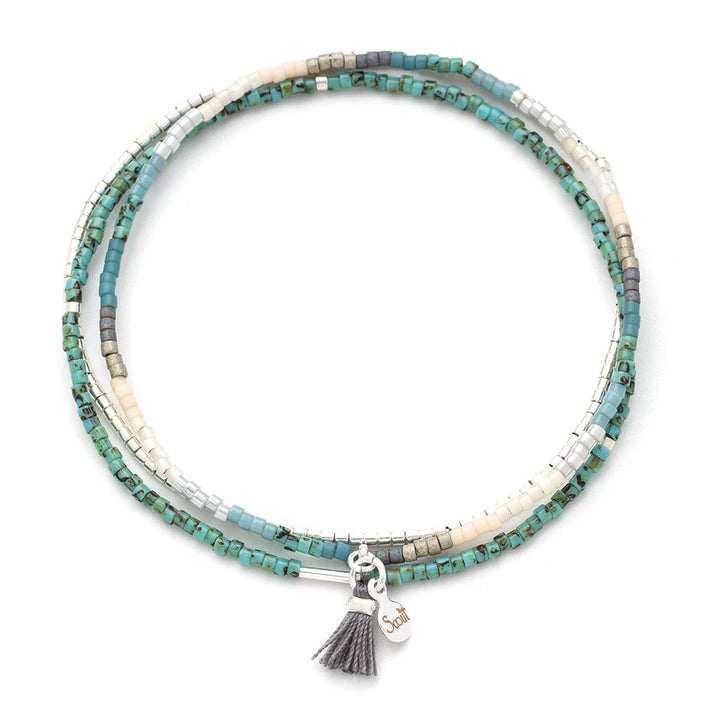 Introducing the Scout Jewelry Turquoise Multi Silver Miyuki Bracelet Trio – a stunning multi-strand beaded bracelet that showcases an array of small, square Miyuki Delica beads in vibrant shades of turquoise, white, and silver. Adorned with a charming grey tassel and a silver tag inscribed with delicate details, this continuous loop design is perfect for those who love stacking bracelets.