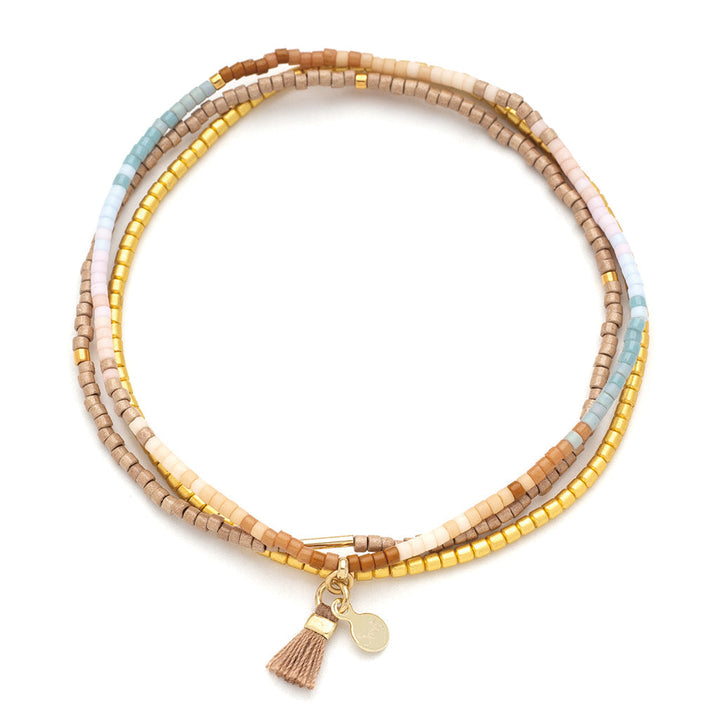 The Desert Multi Gold Miyuki Bracelet Trio by Scout Jewelry features a wrapped design crafted with multicolored Miyuki Delica beads in shades of brown, gold, white, and turquoise. Adorned with a tiny 14K gold charm and a beige tassel, this bracelet set is perfect for stacking to create your unique style.