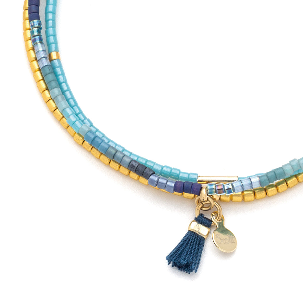 Introducing the Cobalt Multi Gold Miyuki Bracelet Trio by Scout Jewelry, showcasing a stunning combination of 14K gold and Miyuki Delica beads in vibrant shades of blue and gold. The piece is elegantly finished with a blue tassel and a delicate gold charm.