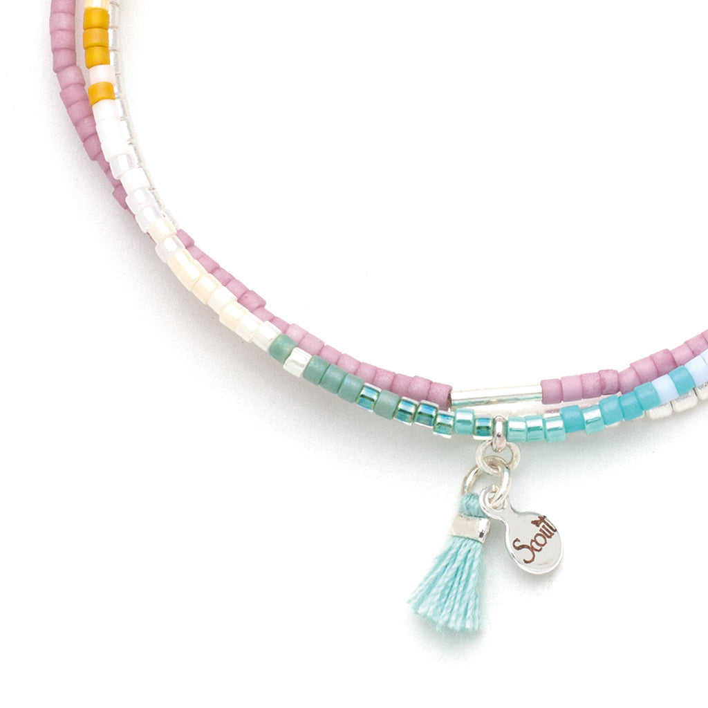 The Bright Multi Silver Miyuki Bracelet Trio from Scout Jewelry is a lively accessory crafted with pastel pink, white, teal, and mustard-hued Miyuki Delica beads. Featuring a small silver charm engraved with "Scout" and adorned with a light blue tassel, this bracelet is perfect for stacking. Its uncomplicated design adds a touch of elegance to any outfit.