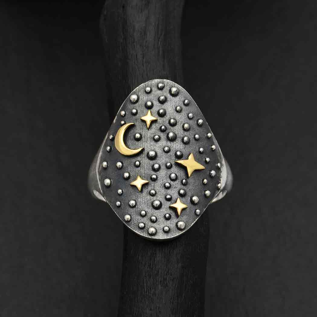 Introducing the s7 Night Sky Ring with Moon and Stars by Nina Designs: This exquisite sterling silver ring showcases a dark, oval face embellished with raised silver dots and intricate gold crescent moon and star designs. The black background enhances its celestial allure, making it an ideal accessory for any stargazer's jewelry collection.