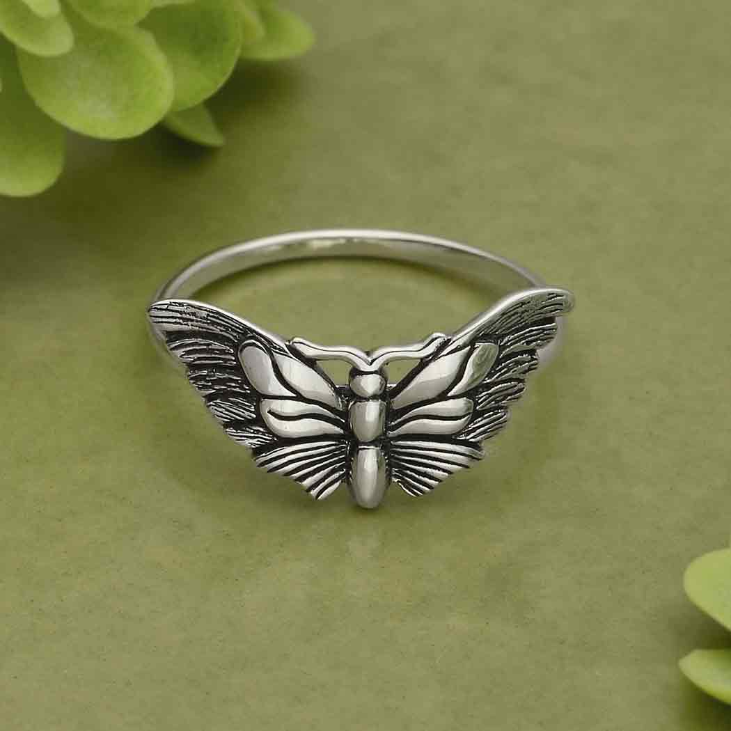 The s7 Winged Butterfly Ring by Nina Designs features an intricate butterfly motif set against a light green backdrop, encircled by vibrant green leaves, making it ideal for those who are passionate about their endeavors.