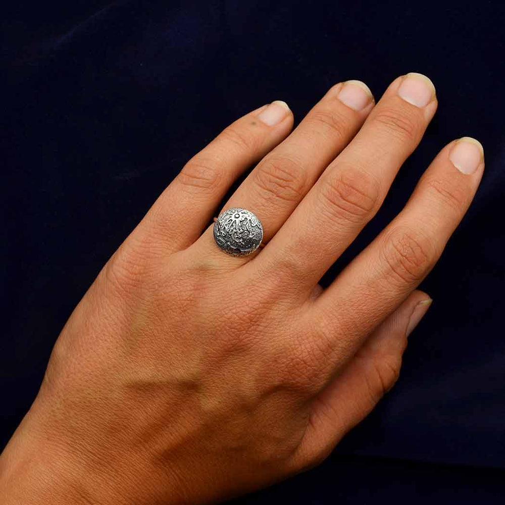 A hand is displayed against a dark background, adorned with the Full Moon Silver Size 7 Ring by Nina Designs on the middle finger. The ring's intricate circular design, reminiscent of a full moon, adds an elegant touch to the simple presentation.