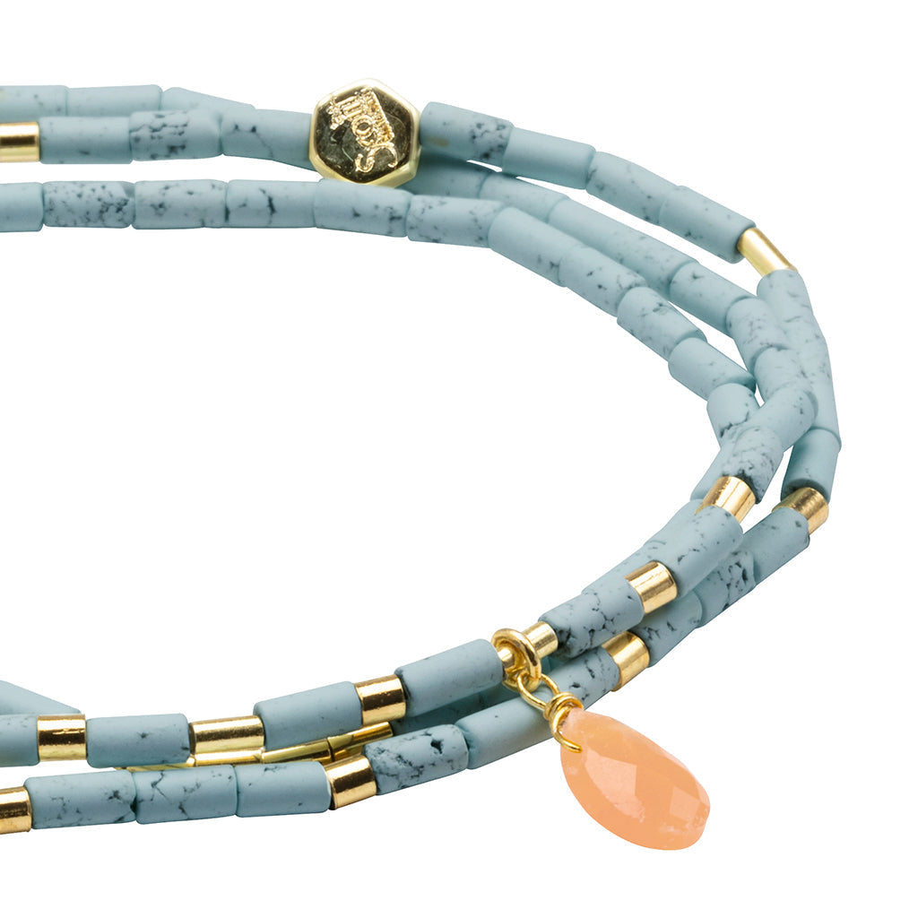 Introducing the Harmony Blue Howlite Gold Teardrop Wrap by Scout Jewelry—a chic layered bracelet adorned with semi-precious pale blue howlite stone beads accented with gold. It features a small hexagonal gold charm and a single faceted peach teardrop pendant for an extra touch of elegance.