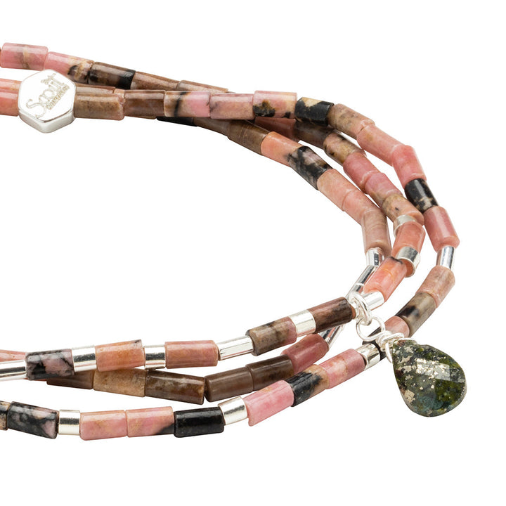 The Healing Rhodonite Teardrop Wrap by Scout Jewelry is a multi-strand bracelet with pink, brown, and black semi-precious stone beads and small silver accents. A teardrop charm with gold pyrite flecks adorns one strand, while the silver clasp features an engraved logo.