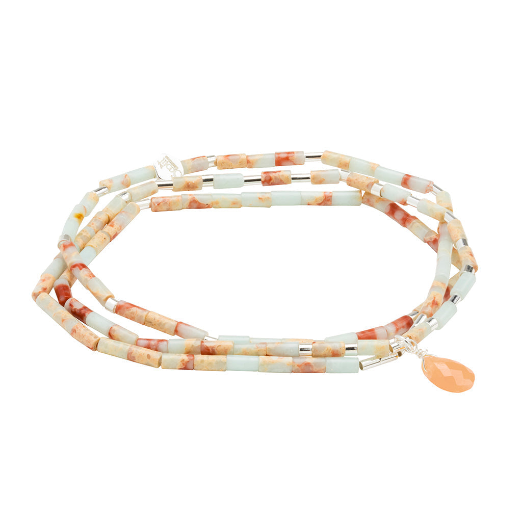 The Peace Aqua Terra Silver Teardrop Wrap by Scout Jewelry is a double-layered beaded necklace featuring cylindrical beads in soft pastel colors, predominantly light blue with apricot hues. It is adorned with a single peach-colored teardrop pendant crafted from semi-precious gemstones, boasting a modern and stylish design.