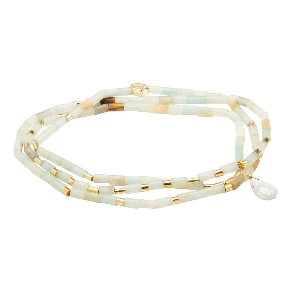 The Courage Amazonite Gold Teardrop Wrap by Scout Jewelry is a delicate beaded bracelet featuring light green, semi-precious amazonite beads, beige cylindrical beads, and small gold spacer beads. The bracelet includes a small gold logo charm and a dangling teardrop-shaped pearl accent.