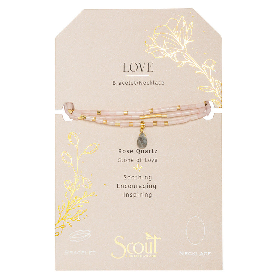 The Love Rose Quartz Gold Teardrop Wrap by Scout Jewelry is a versatile bracelet/necklace with pink rose quartz and gold accents, known for soothing, encouraging, and inspiring qualities. It features semi-precious stone beads on a beige card with floral designs.