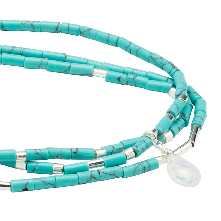 A close-up of the Scout Jewelry "Calm Turquoise Silver Teardrop Wrap" necklace, showcasing semi-precious turquoise cylindrical beads and small silver spacers, with an opalite teardrop-shaped white pendant.