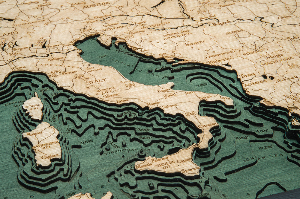The WoodChart Western Europe Chart (24.5" x 31", Black Frame) features a detailed wooden map of Italy and nearby countries, with engraved labels, raised land contours, and carved layers showing the Mediterranean Sea.