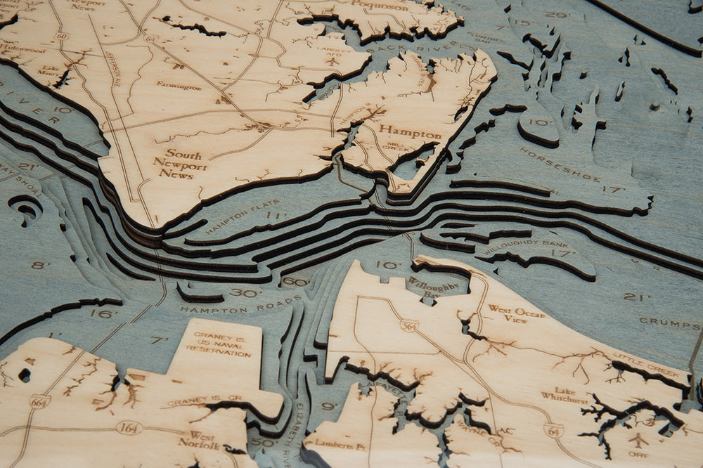 A close-up of the WoodChart Norfolk VA 24.5 x 31 White Frame map reveals detailed layered wood cutouts illustrating Hampton Roads’ land and water features, with engraved place names and geographic details.