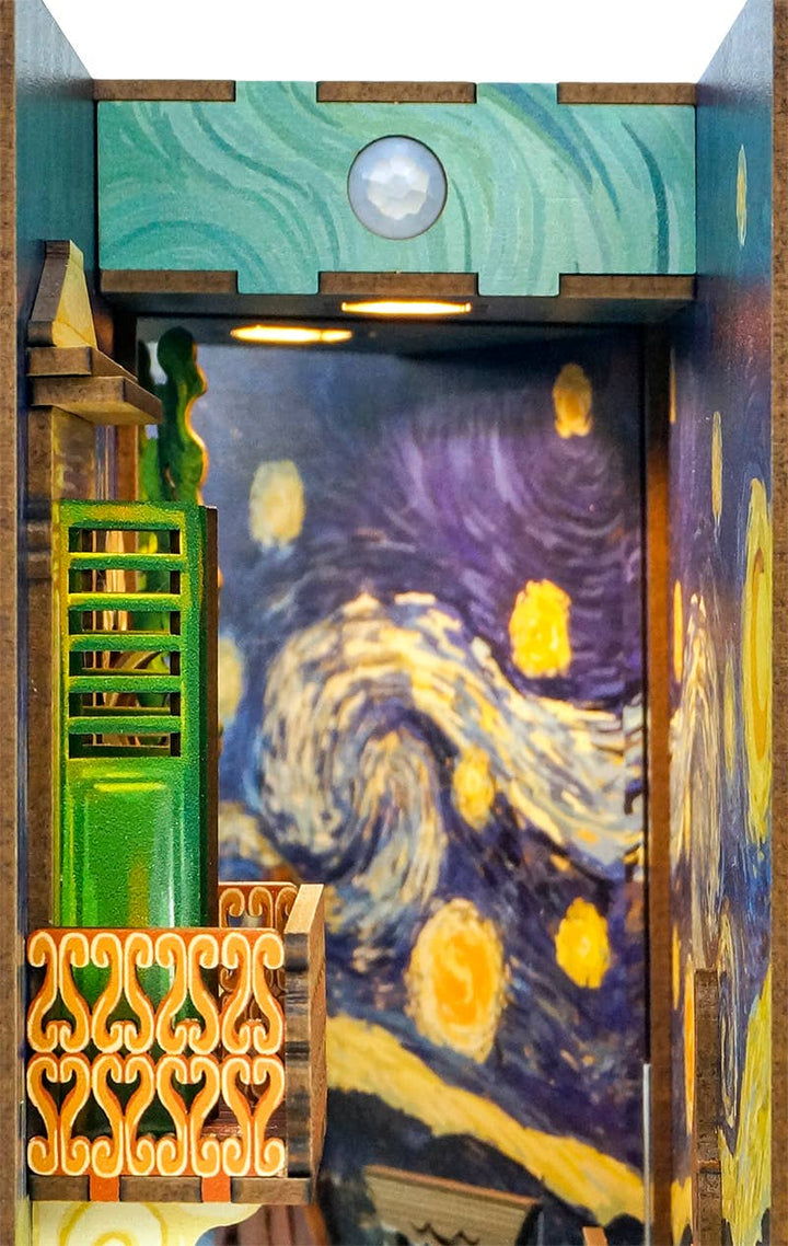 The DIY Book Nook Kit: Vincent's World by Hands Craft is a Van Gogh-inspired bookshelf insert with a green balcony and orange railing, set against a "Starry Night"-themed backdrop featuring swirling blue, yellow, and white patterns.