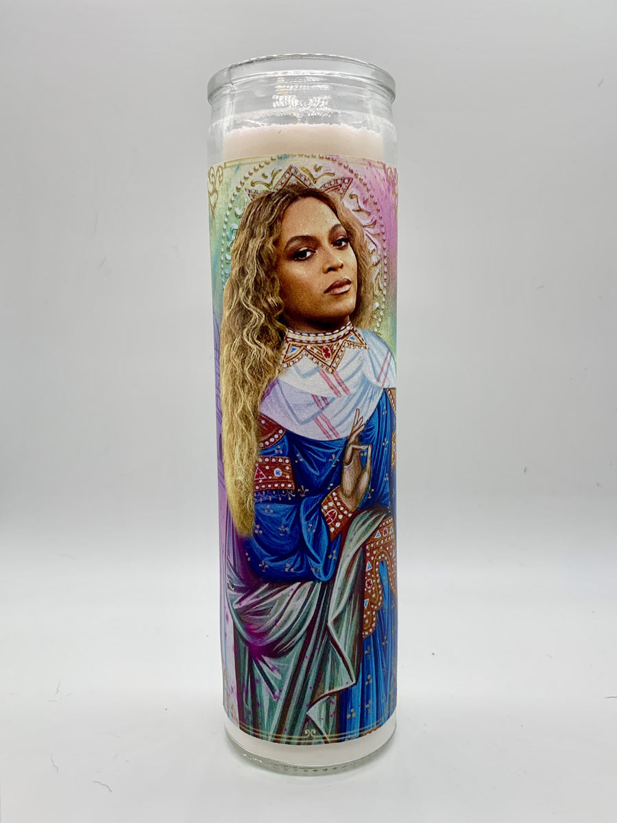 The unlit tall, hand-poured Beyonce Candle by BOBBYK BOUTIQUE showcases an illustration of a woman with long blonde hair in a blue and red intricately designed robe, evoking religious iconography.