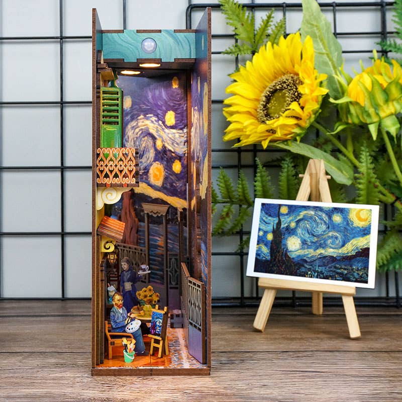 The Hands Craft DIY Book Nook Kit: Vincent's World is a miniature diorama inspired by Van Gogh’s "Starry Night," featuring café figures, a sunflower, green ferns, and a small easel with the iconic artwork for a charming bookshelf display.