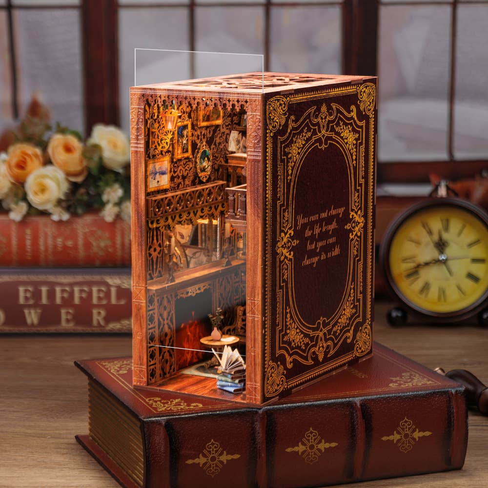 The Hands Craft DIY Book Nook Kit: Eternal Bookstore with Dust Cover is a detailed miniature room set inside a wood book-shaped box with gold designs, featuring shelves, furniture, soft lighting, flowers, and a clock—perfect as a literary gift.