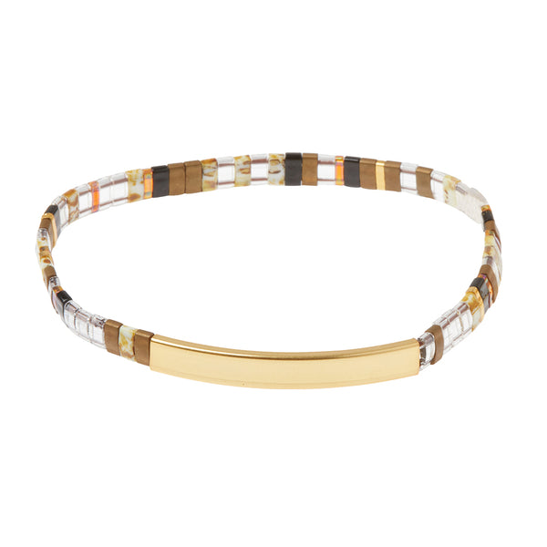 The Miyuki Sparkle and Shine Topaz Gold bracelet by Scout Jewelry captivates with its small, colorful beads in shades of brown, gold, and translucent. A sleek 14K gold dipped bar accent adorns the center, elegantly wrapping around the wrist to exude a touch of empowerment and style.