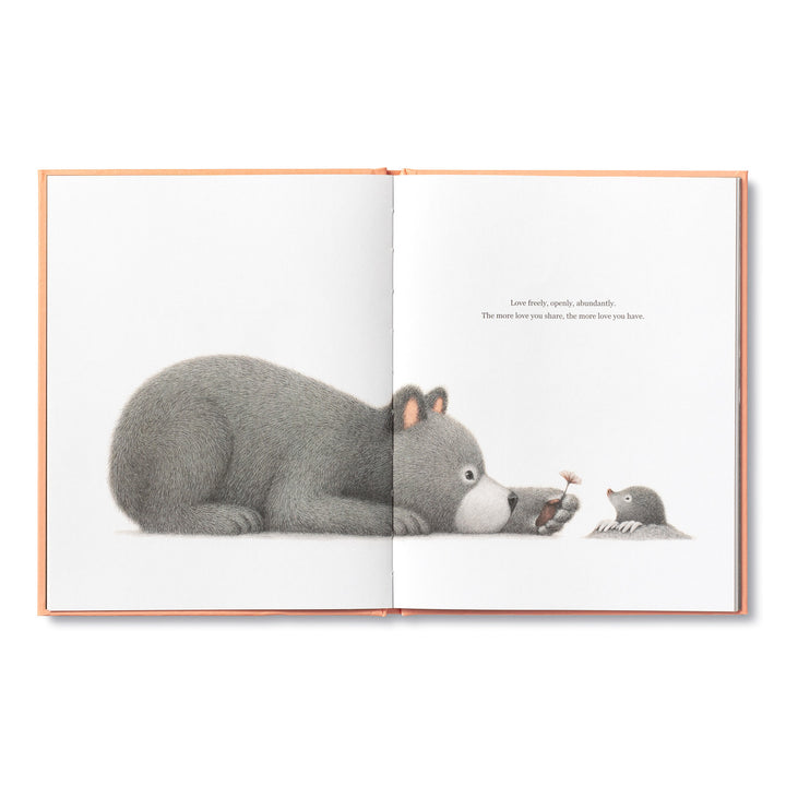 An open illustrated children's book titled "Feeling Grateful" by Compendium depicts a gray bear lying down on the left page, gazing at a small mole holding a flower on the right page. The text reads, "Love freely, openly, abundantly. The more love you share, the more gratitude and joy you receive.