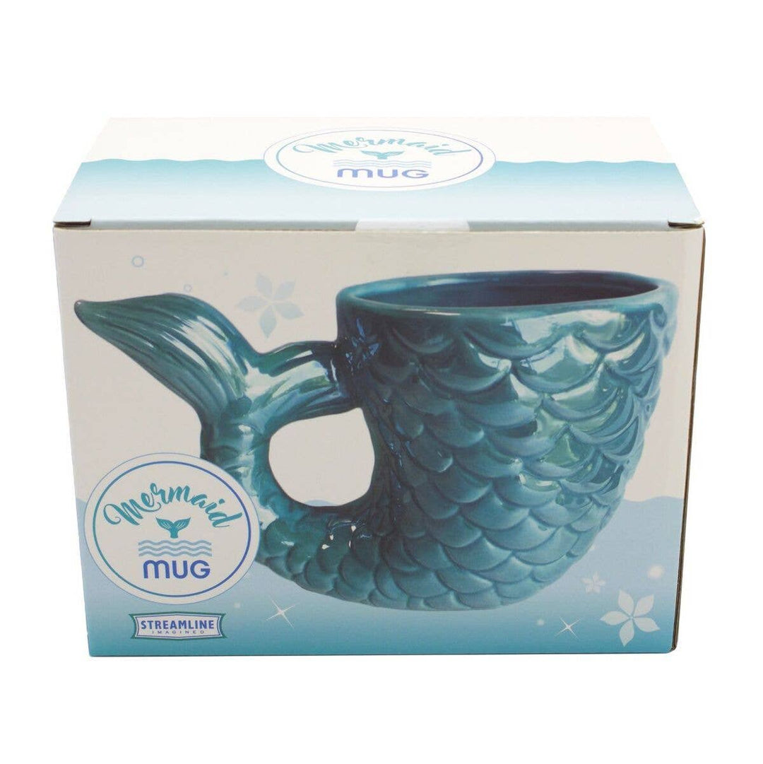 The image showcases a product box with an illustration of a ceramic mug resembling a mermaid tail. This detailed product description highlights the aqua-blue mug with a scale pattern and a fin-inspired handle. The box prominently displays "Streamline Mermaid Tail Mug.