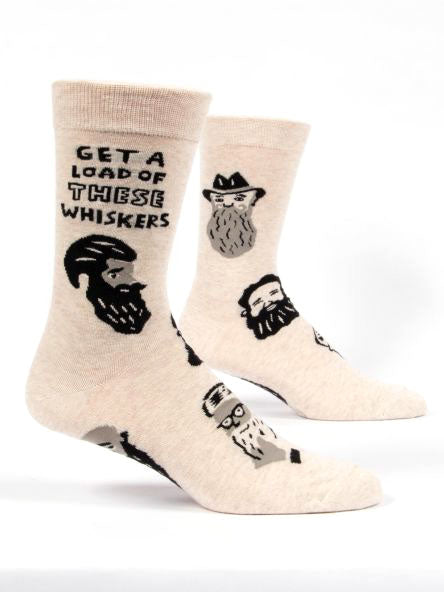 Blue Q's “Get a load of these whiskers” socks feature various illustrations of bearded faces on a cream-colored background. Made from combed cotton, these men's socks showcase the text "GET A LOAD OF THESE WHISKERS" at the top and depict different beard styles, with some characters donning cowboy hats and glasses. They fit shoe sizes 7-12.