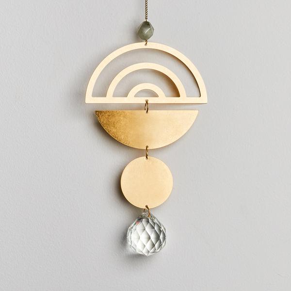 Introducing the Rainbow Labradorite Suncatcher by Scout Jewelry, a minimalist hanging ornament showcasing a geometric design. This crystal decoration comprises a semi-circle with arches on top, a golden half-circle in the middle, a solid golden circle at the bottom, and a faceted clear crystal as its finishing touch. All elements are intricately connected by small metal links.