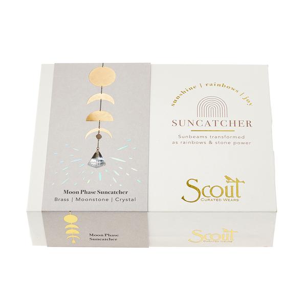 A box containing the Moon Phase Moonstone Suncatcher features elements of brass, moonstone, and semi-precious gemstones. The packaging displays an illustration of a suncatcher with the brand name "Scout Jewelry" and includes slogans about sunshine and rainbows.