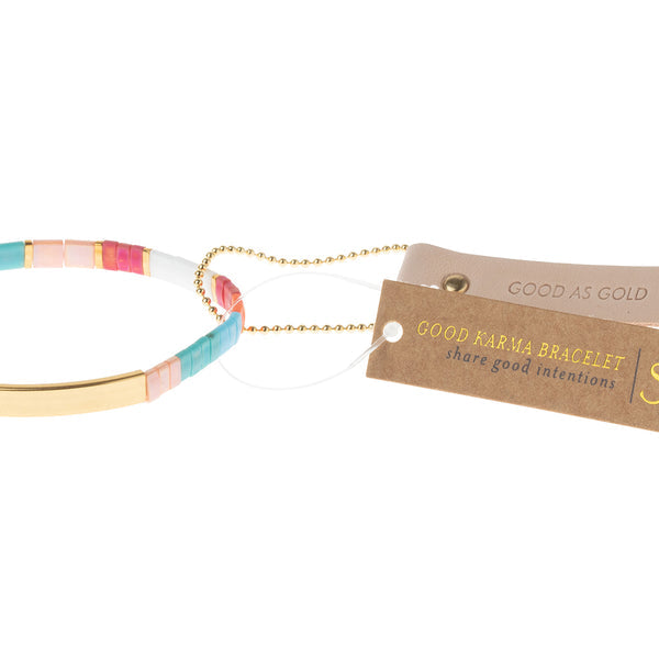The Miyuki Good As Gold Gold bracelet by Scout Jewelry features alternating rectangular beads in vibrant shades of pink, gold, teal, and white. Highlighted with a 14K gold-dipped bar, it is secured on a string adorned with a tag that reads "Good Karma Bracelet - Share good intentions." This bracelet stands out beautifully against the white background.