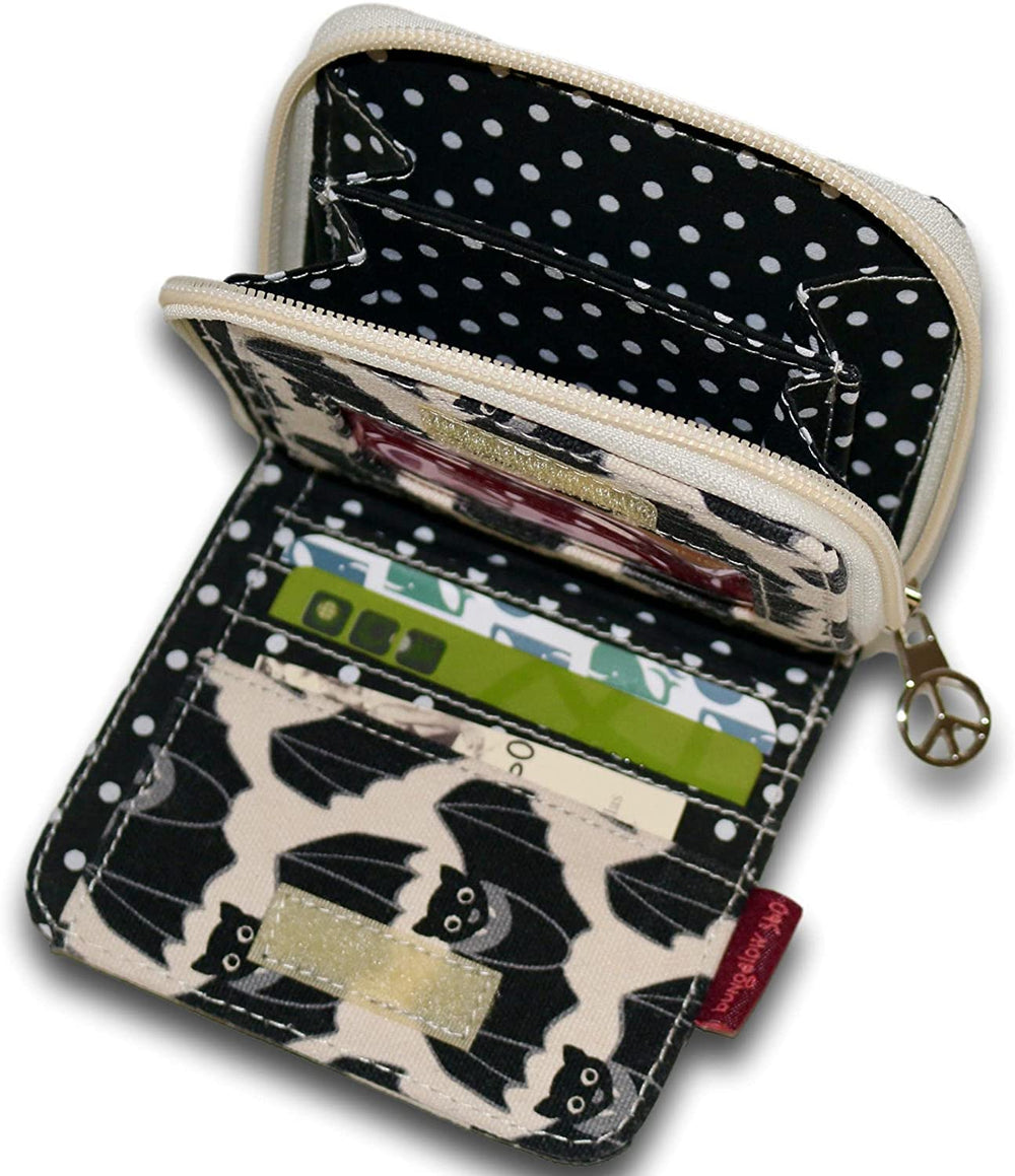 The Bill Fold Wallet Bat by Bungalow 360 is open, revealing multiple compartments. Crafted from vegan cotton canvas, this small wallet features a black and white polka dot interior. The exterior design showcases unique black bat patterns. Credit cards and an ID card are visible in the card slots, and a zipper compartment with a peace sign zipper pull provides additional storage.