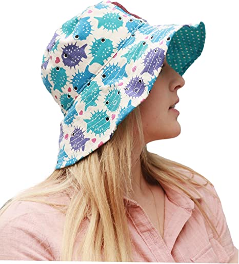 A woman with long blonde hair, shown in profile, wears a pink shirt and the Bungalow 360 Beach Hat Puffer Fish, a reversible beach hat featuring unique blue and purple pufferfish designs.