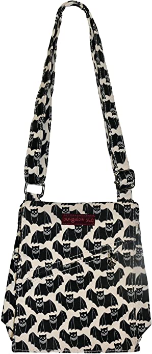 Introducing the Sm Messenger Bat by Bungalow 360, a shoulder bag crafted from natural durable cotton canvas and adorned with a unique black and white bat pattern. The strap and body of the bag feature this same distinctive design, complemented by a maroon label with white text near the top center. An adjustable buckle on the strap adds practicality to its stylish appearance.